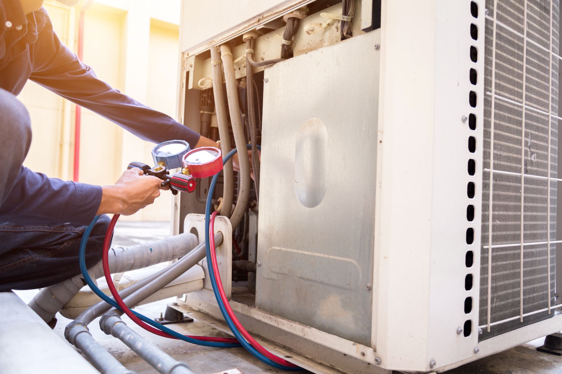 Technician using pressure gauges on air conditioning unit outdoor condenser
