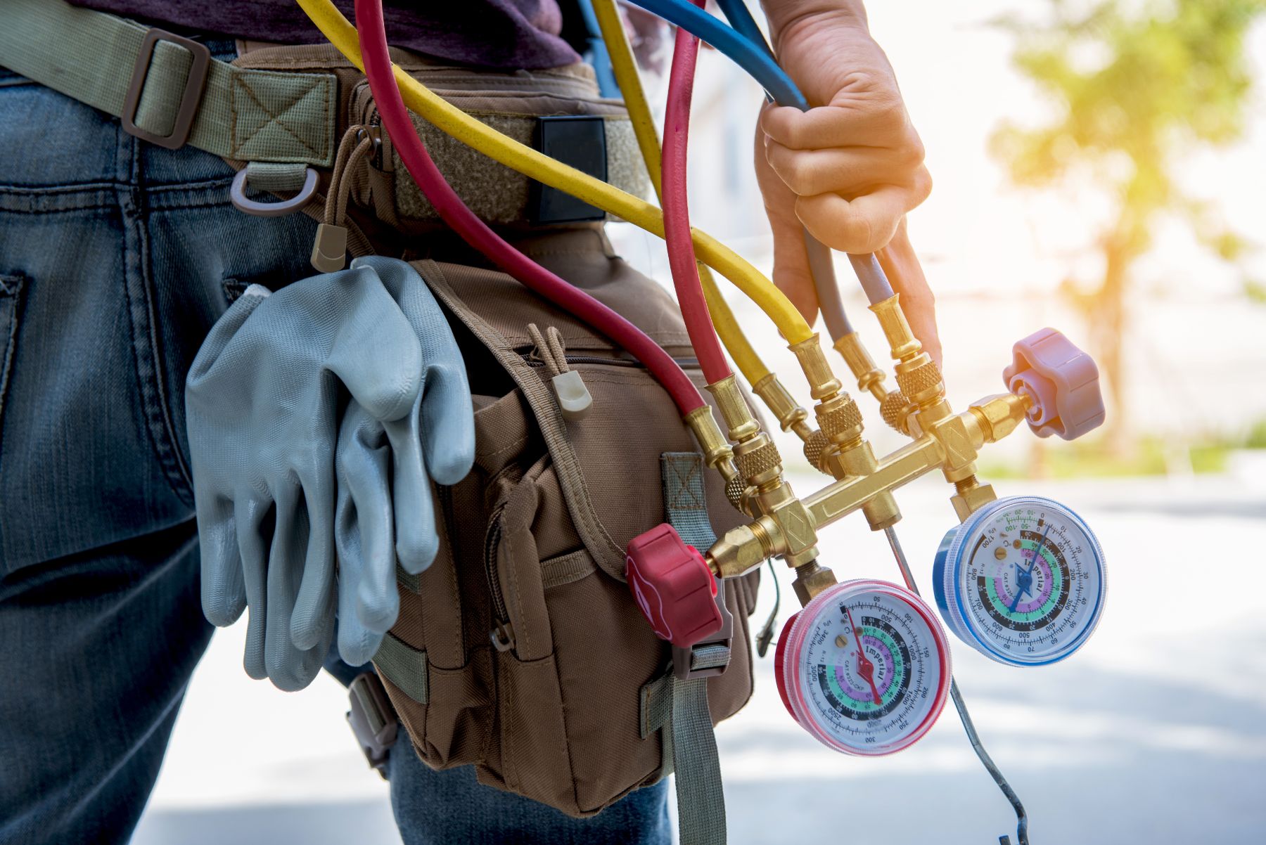HVAC technician holding pressure gauges and hoses with service belt and work gloves