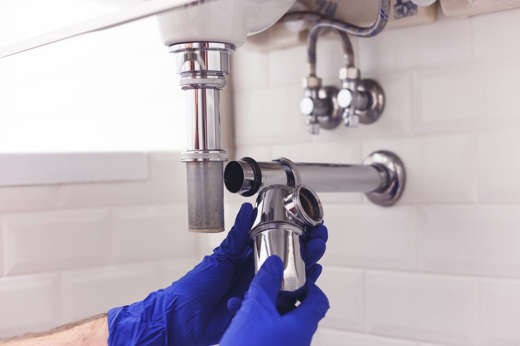 Plumber in blue gloves installing chrome P-trap under sink