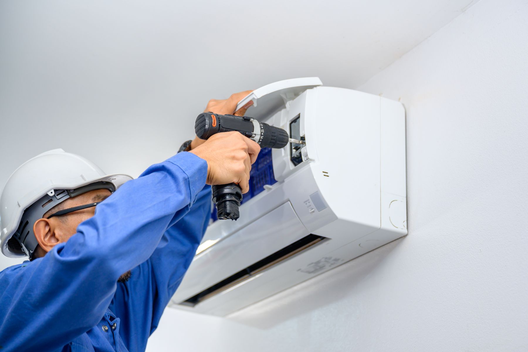 Technician in blue uniform installing or servicing white wall-mounted air conditioning unit