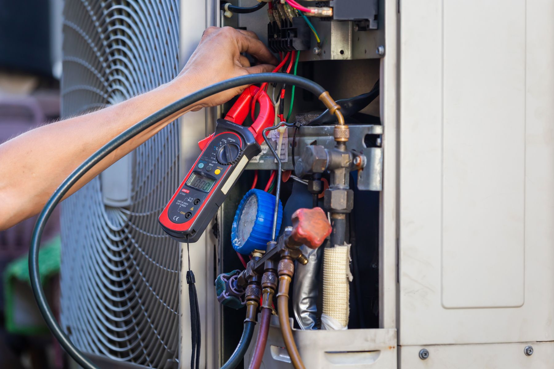 Technician using red clamp meter to test electrical connections in HVAC unit