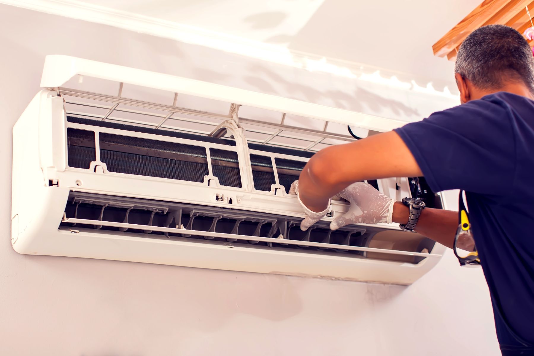 Technician in protective gloves servicing an open wall-mounted air conditioner unit