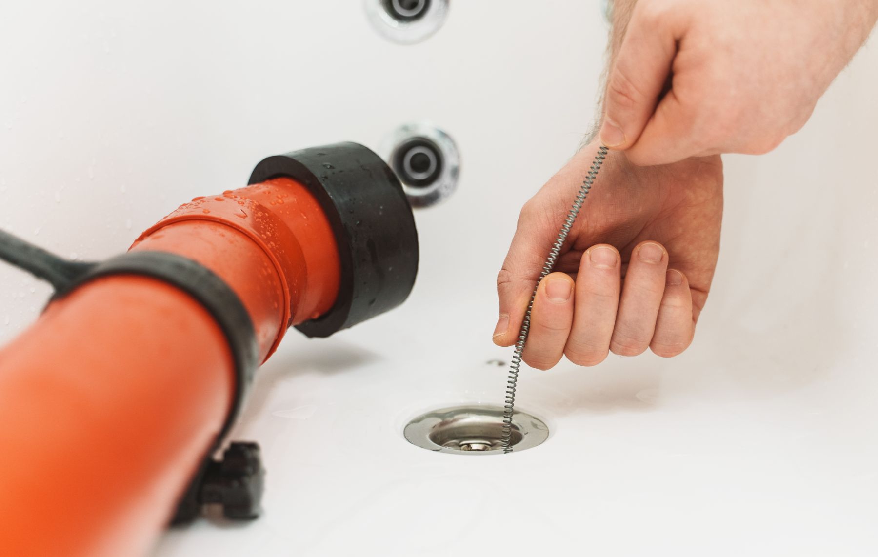 Person using orange plumbing snake to clear drain opening in white ceiling