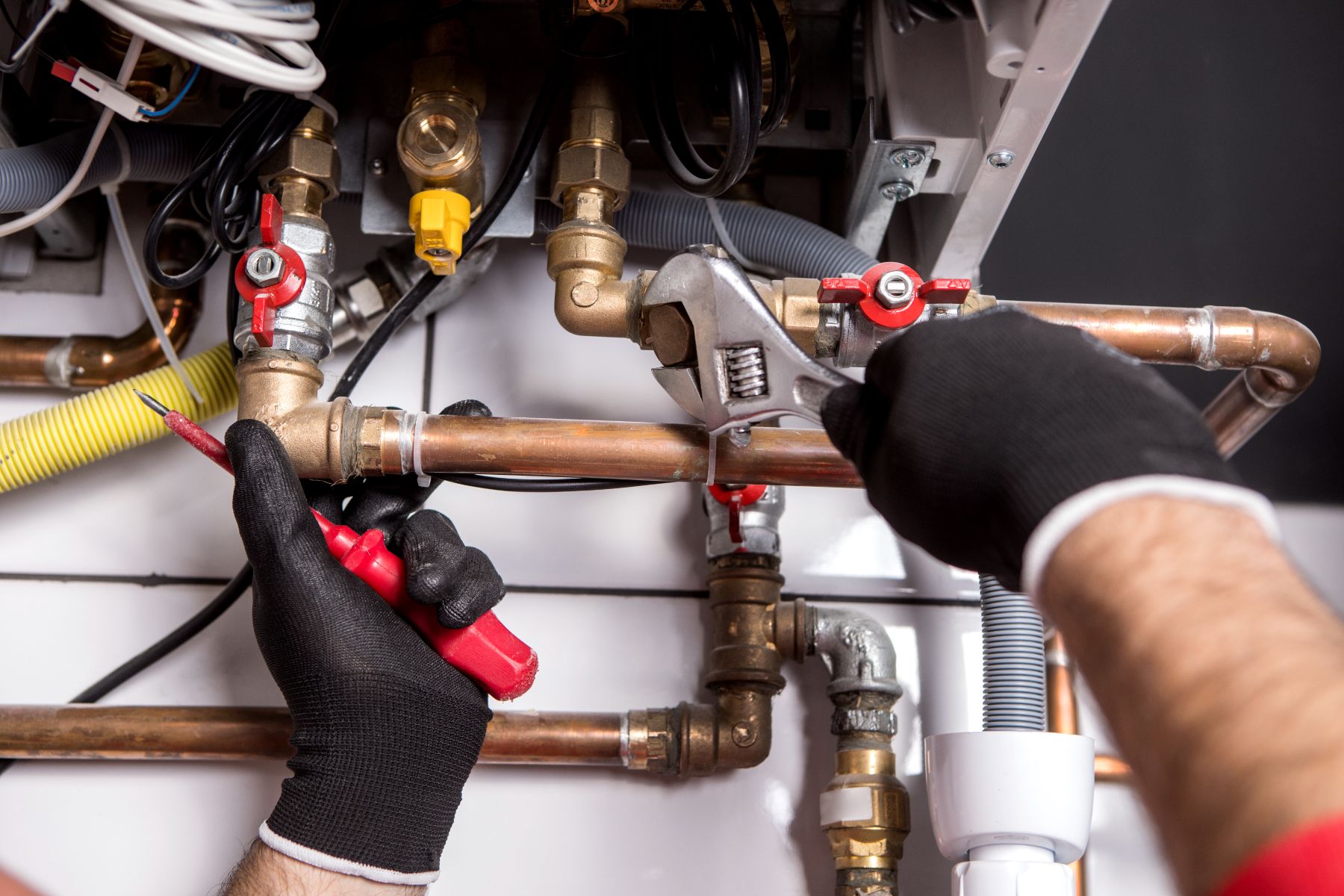 Plumber in black gloves using wrench on copper pipes and brass valves