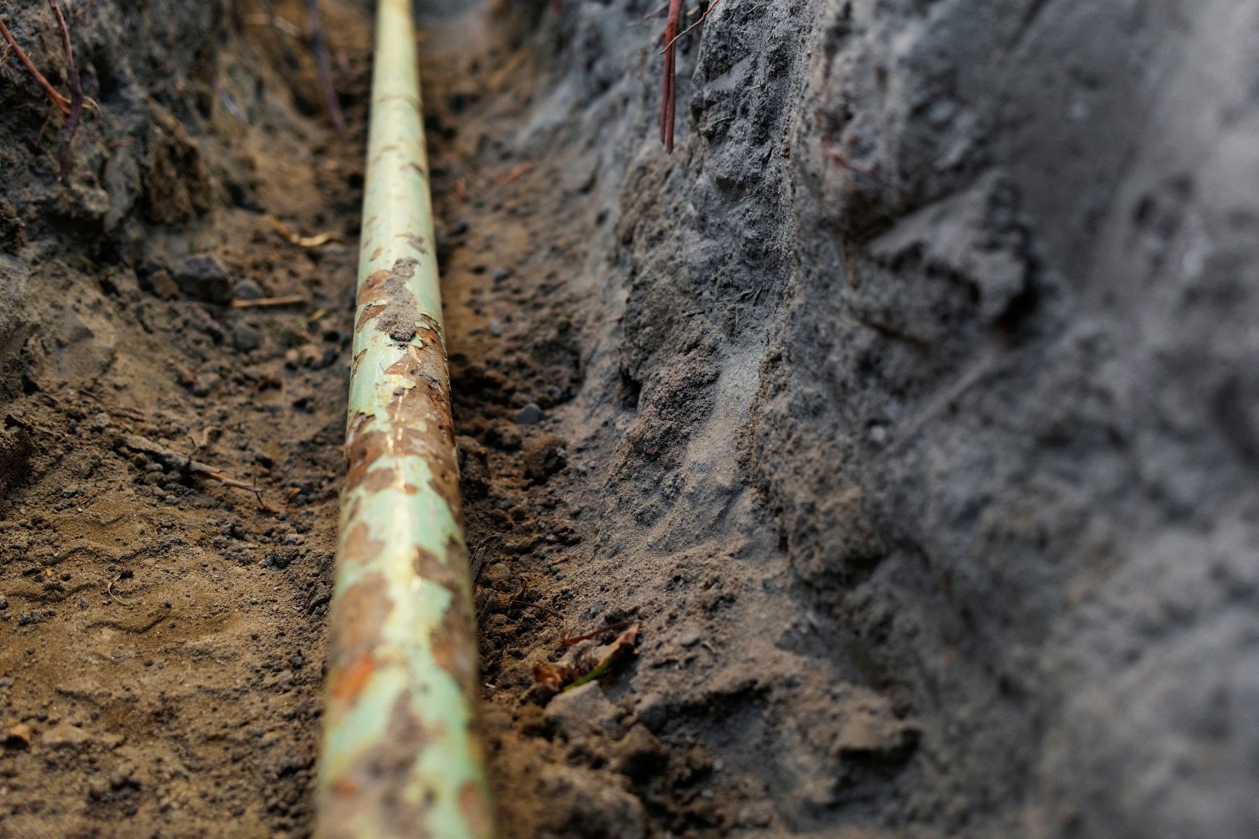 Corroded metal pipe buried in soil next to concrete foundation