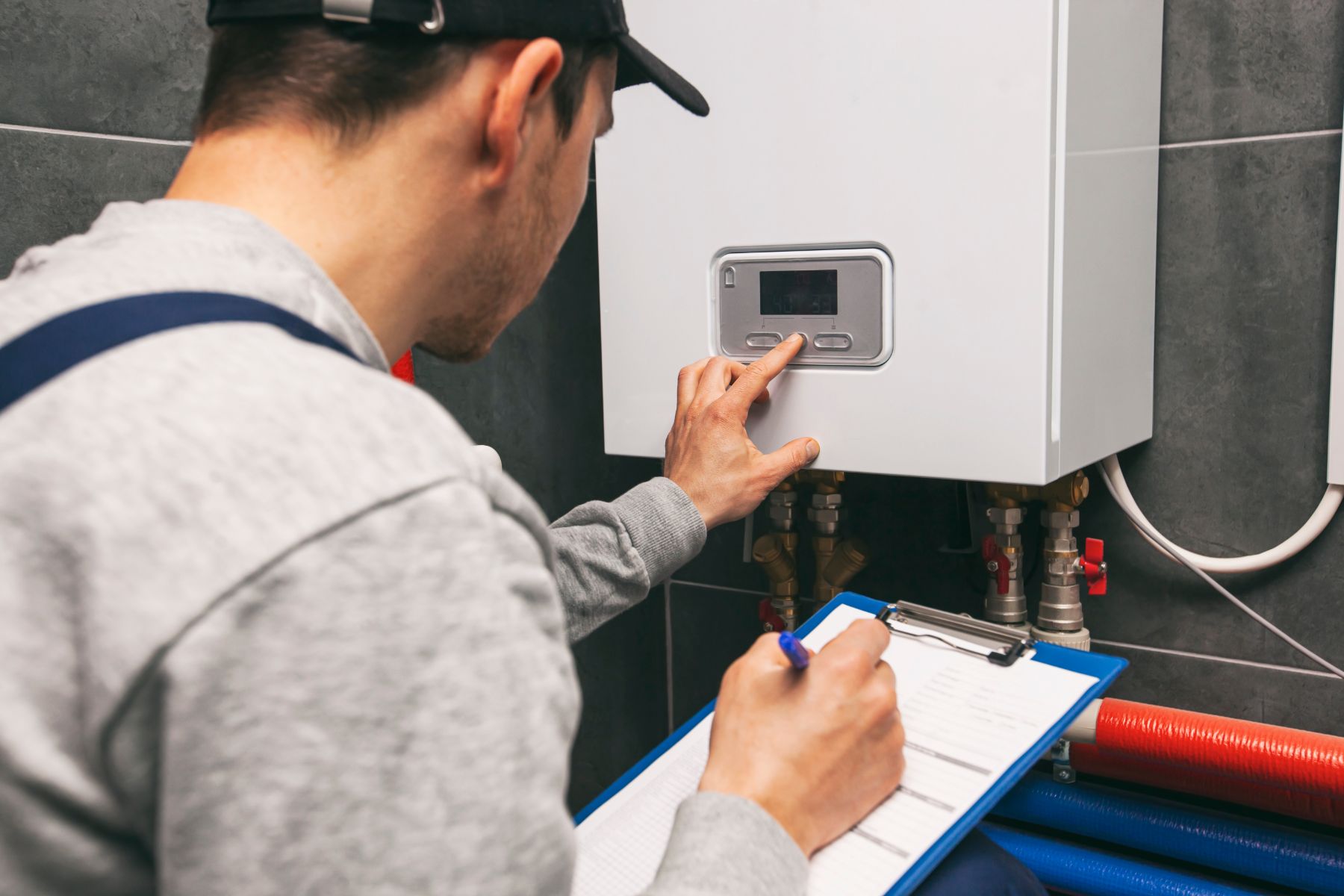 Technician inspecting wall-mounted boiler thermostat while taking notes on clipboard