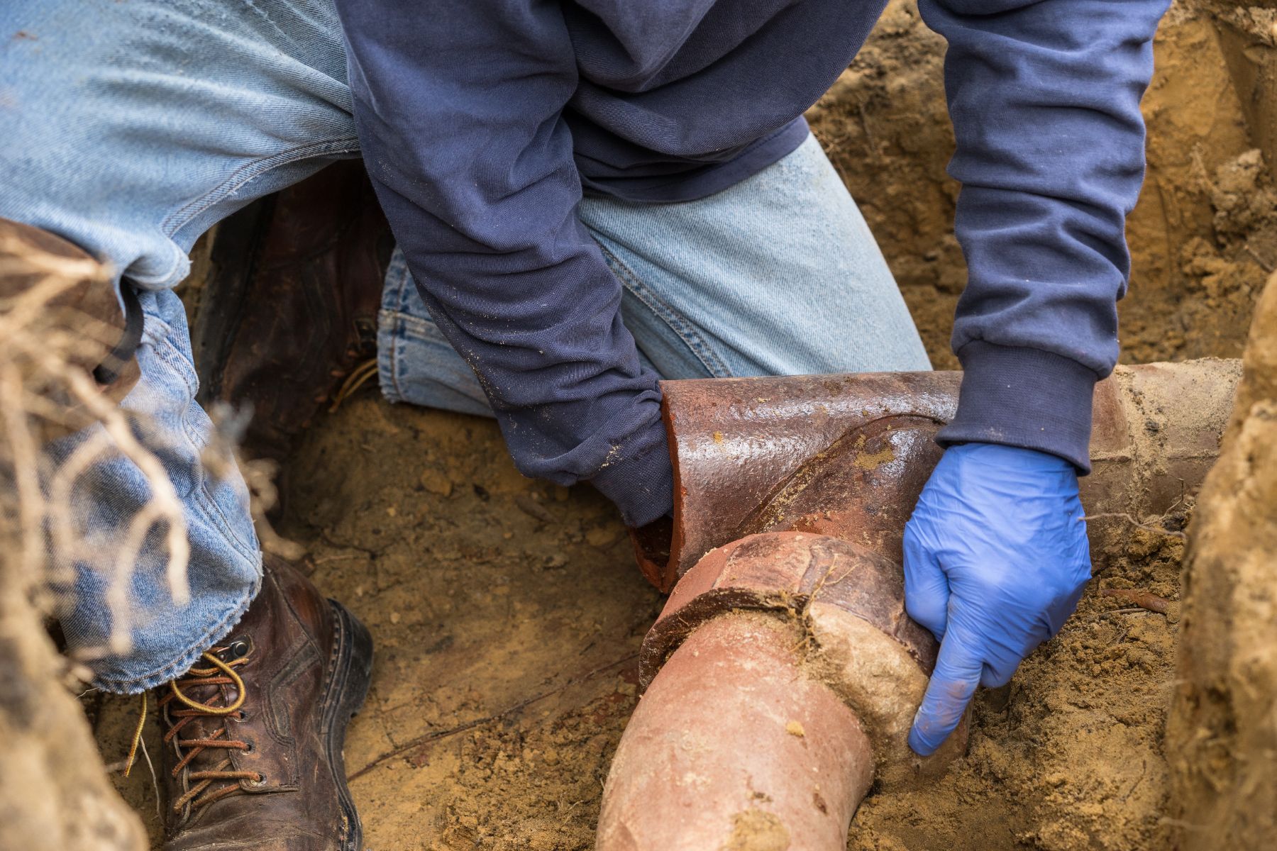 Archaeologist in blue gloves examining terracotta artifact in excavation trench